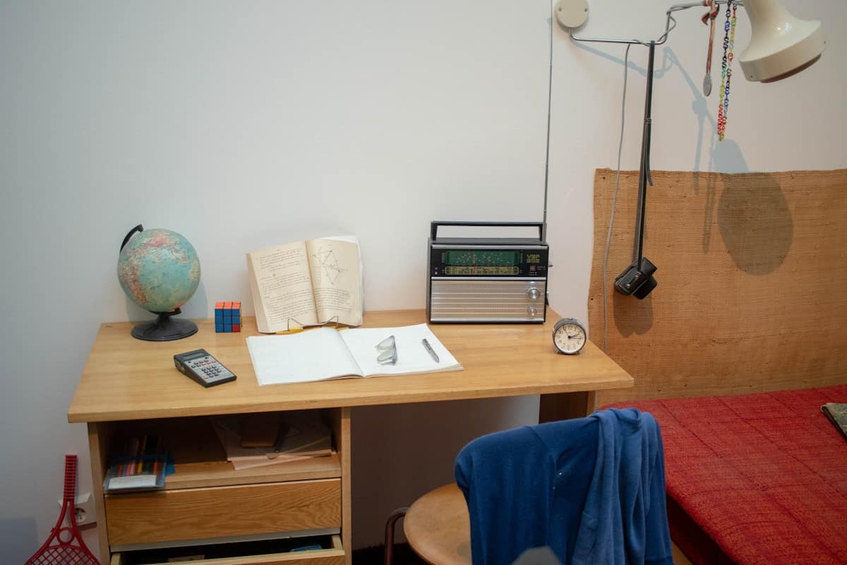 Escritorio de madera con un globo terráqueo, un libro abierto, un cuaderno, una calculadora, una radio antigua y un despertador.